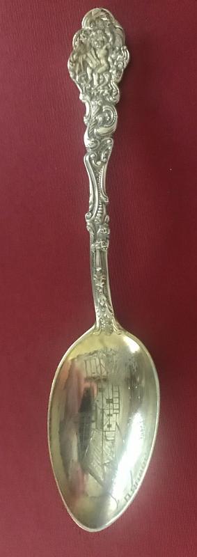 Souvenir Mining Spoon Oronogo No. 1 Mine, Oronogo, Jasper Co.,  MO.JPG - SOUVENIR MINING SPOON ORONOGO MINE NO 1 ORONOGO MO [Sterling silver spoon, 5 7/8 in. long, engraved mining scene in bowl, bowl marked OROGONO NO. 1, handle front in ornate Versailles pattern introduced in 1888 by Gorham;  It shows an angel holding a musical instrument, maybe pipes or a lyre; reverse is marked with the old lion-anchor-G  hallmark for Gorham, K in a square shape and Sterling; weight 30.9 gms. [Eight miles north of Joplin, Missouri stands the village of Oronogo, originally named Minersville when it sprang up in 1850. According to legend, a miner dug there with his pick and shovel and said, "It's ore here or no go," and so the name Oronogo stuck. Nearby is the site of the richest lead and zinc strike ever made in southwest Missouri. Tom Livingston first discovered the mine before the Civil War, but renegades stole his land while he was away fighting. After the war, they sold it to Granby Mining Company for $50. After almost 80 years of continuous operation, the mine produced $30 million worth of lead and zinc. The Oronogo Circle Mine No. 1, one of the few open-pit mines in the district, stretched 300 feet deep and 600 feet across. The 12-acre unroofed cavern was strip mined at three levels-150 feet, 240 feet, and 360 feet--a flurry of activity with men, trucks, and machinery going up and down the steep inclines. Numerous mills serviced the operation. The largest chunk of pure lead ever found in the district came from the Oronogo Circle. Two flat cars carried it to the World's Fair in Chicago in 1893. After the exhibit ended, the mammoth rock sold for $6,000. A deadly accident occurred at the mine in 1901 when a blast of dynamite detonated prematurely, killing 12 men and wrecking a $50,000 mill. Operations shut down for several months because miners refused to go back to work. Chicago capitalists ran the mine from 1906 to 1914, raking in profits of $3 million. They sold it to the Connecticut Mining Company for $500,000. The ground was so honeycombed with shafts and drifts at four levels that it was no longer safe to work underground. In an ill-fated endeavor to make mining the Circle safer, the new owners closed the old shafts and dismantled 20 small mills. They removed underground support pillars and stripped the entire tract down to 300 feet, using the largest steam shovels available. Then they buried dynamite at the former mill sites and ignited them all at once, causing a blast that almost blew Oronogo off the map. The ground shook so violently that a new mill, built on solid ground, fell into the pit and killed six men. The catastrophe cost the company more than $1 million. Connecticut Mining went out of business, and the mine reverted to its original owner, the Granby Mining Company. For many years, the tract lay idle, although investors made half-hearted attempts to resume strip mining. By the 1970s, the huge water-filled pit had become popular with scuba divers, who liked to explore its depths, yet even that turned out tragically, with the deaths of some of the divers.]